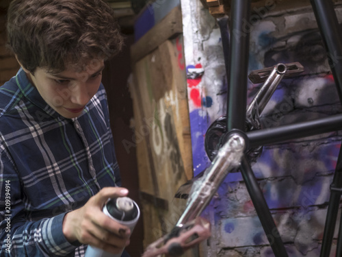 close up young man painting the bmx bicycle with spray can in the workshop