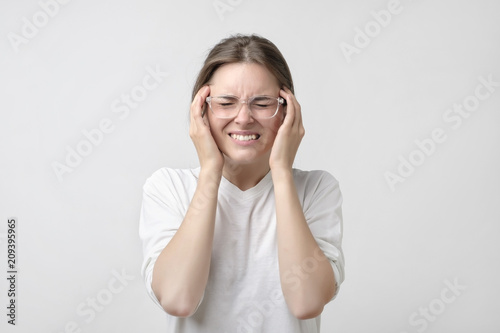 European girl in white t-shirt suffers from terrible headaches and compresses the head with fingers.