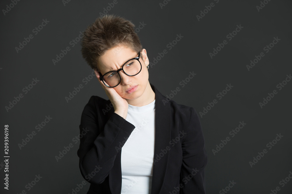 beautiful young girl with short hair, in a black suit and wearing glasses on a black background with a tired expression beautiful young girl with short hair, in a black suit and wearing glasses on a black background with a tired expression