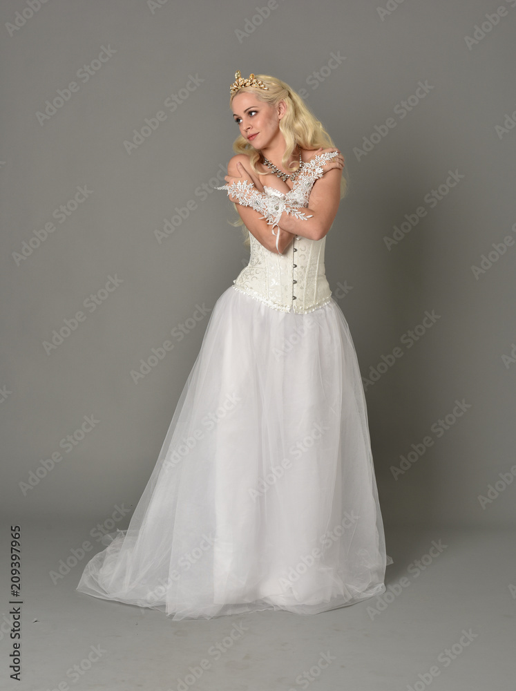 full length portrait of blonde girl wearing white corset gown. standing pose on grey studio background. full length portrait of blonde girl wearing white corset gown. standing pose on grey studio background.