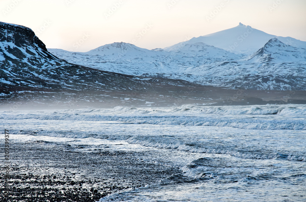 Amazing winter landscape with black beach, ocean and Snæfell volcanic mountain in the background
