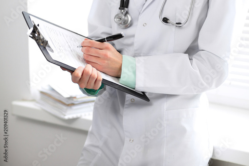 Female doctor filling up medical form on clipboard closeup.  Healthcare, insurance and medicine concept photo