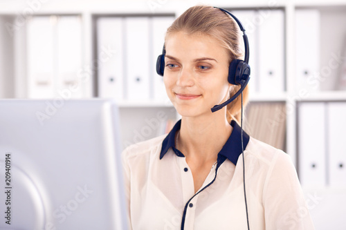 Call center operator. Blonde business woman in a headset in white office with pc computer