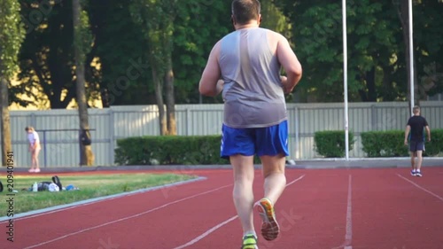 Fat man running around the stadium. Back view. Slow motion photo