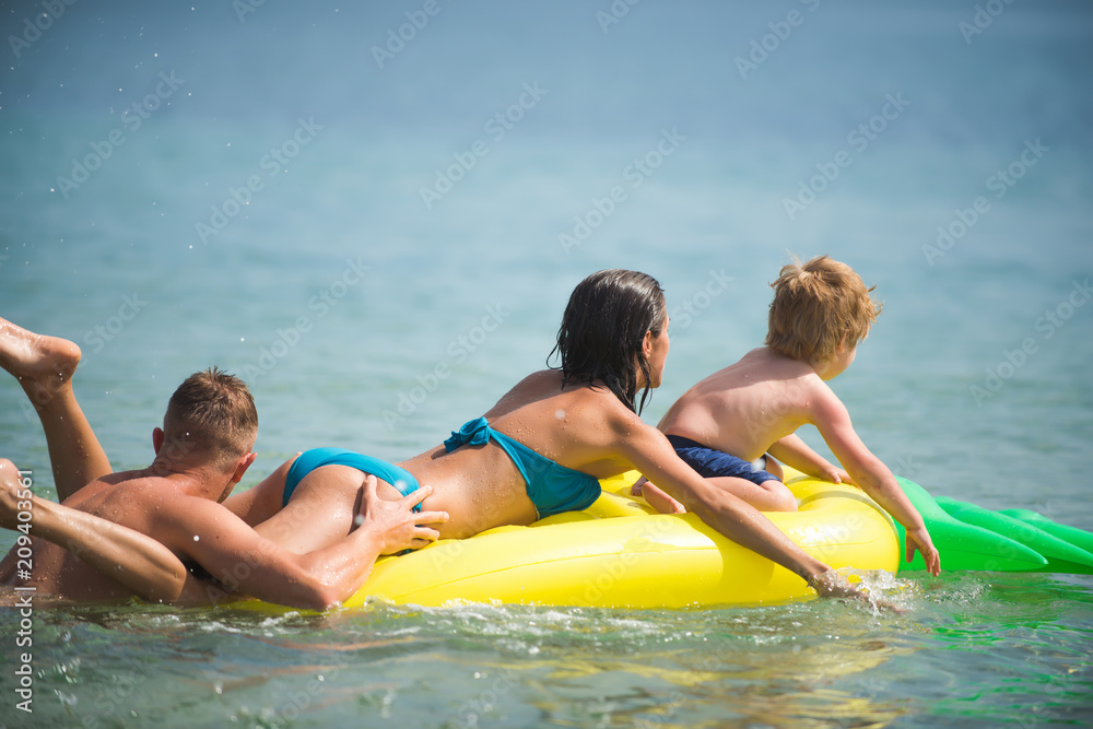 Obraz premium Summer vacation and travel to ocean. Happy family couple on Caribbean sea. Father and mother with son play in water. Pineapple inflatable or air mattress. Maldives or Miami beach activity joy
