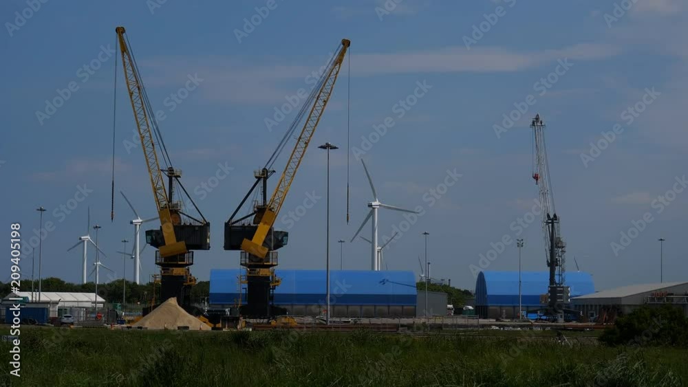 Industrial area on a seaside in Northwest of England, UK. Wind farm turbines spinning behind two cranes for unloading barge freight Industrial area on a seaside in Northwest of England, UK. Wind farm turbines spinning behind two cranes for unloading barge freight