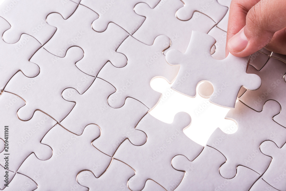 Hand holding pieces of jigsaw puzzle and insert into the missing hole Hand holding pieces of jigsaw puzzle and insert into the missing hole