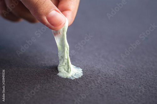 Fotografi Hand removing sticky chewing gum from black textile or clothes