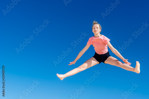 ein junges Mädchen springt vor blauem Himmel im Spagat hoch in die Luft