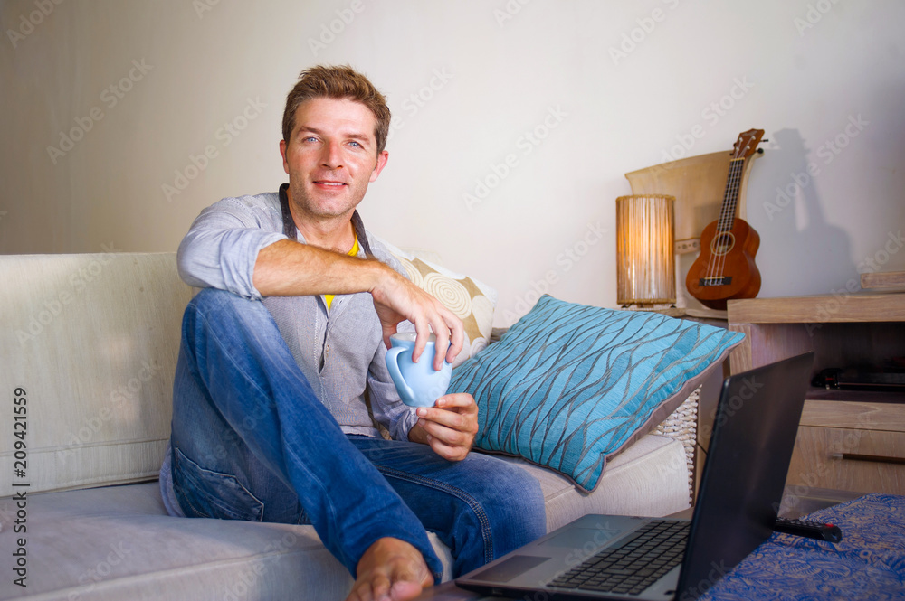 young attractive and successful man working from home living room sitting on couch networking on laptop computer drinking coffee happy in freelancer young attractive and successful man working from home living room sitting on couch networking on laptop computer drinking coffee happy in freelancer