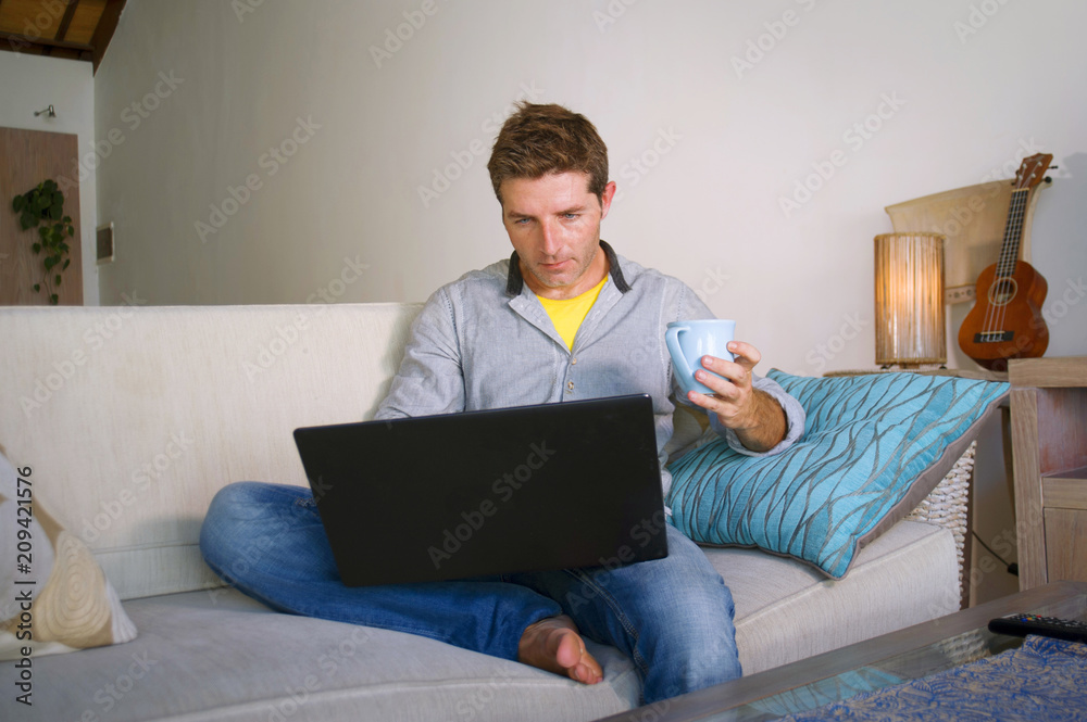 young attractive and successful man working from home living room sitting on couch networking on laptop computer drinking coffee happy in freelancer concept young attractive and successful man working from home living room sitting on couch networking on laptop computer drinking coffee happy in freelancer concept