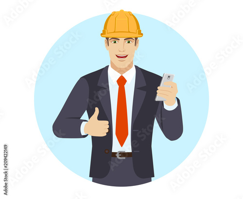 Businessman in construction helmet with mobile phone showing thumb up