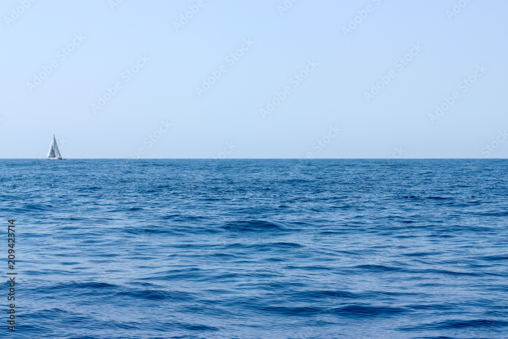 Fototapeta premium Sea water landscape with dark waves and a lonely white yacht at the horizon on sunny day.