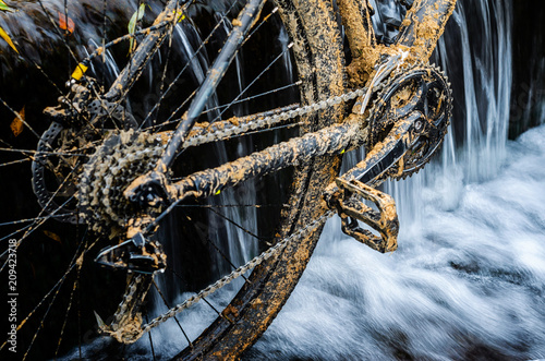 Dirty Mountain Bike Stands in a Creek Against the Small Waterfall. Dirty Chain Drive Mountain Bike close-up. Cleaning a Bicycle Concept