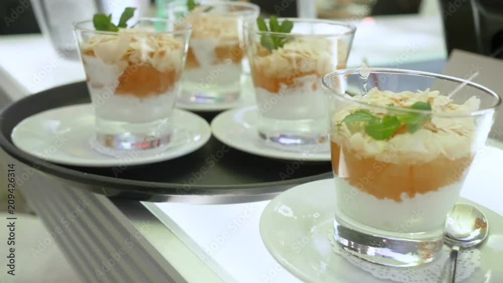 Cream dessert with the addition of various jams of berries, decorated with flakes of almond arecha and mint. Slider camera, close-up, in a glass cup. A bar in the restaurant, before serving guests Cream dessert with the addition of various jams of berries, decorated with flakes of almond arecha and mint. Slider camera, close-up, in a glass cup. A bar in the restaurant, before serving guests