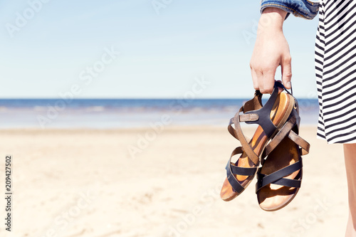 Woman on the beach holding her sandals at sunny summer day photo
