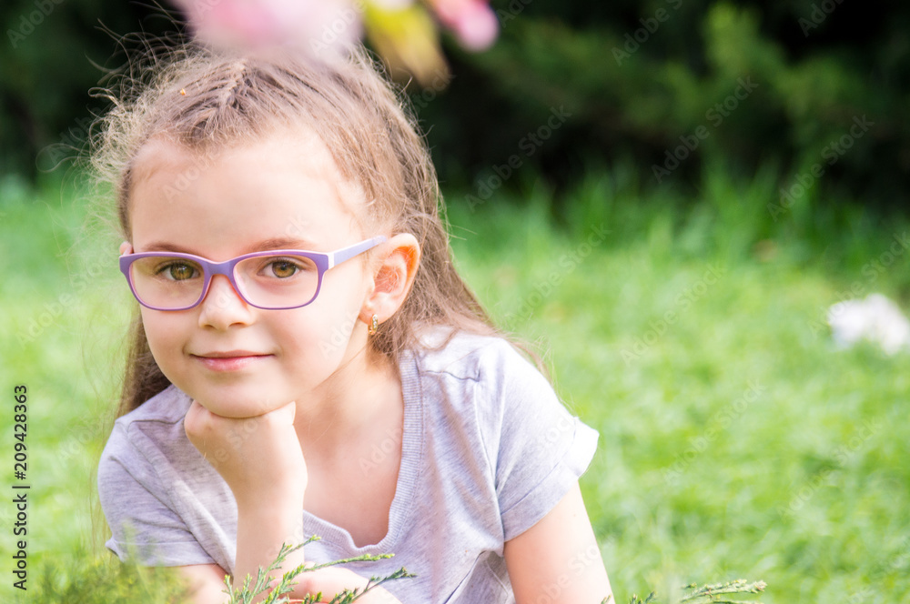 portrait of a six year old girl with glasses on a blurred background of greenery portrait of a six year old girl with glasses on a blurred background of greenery
