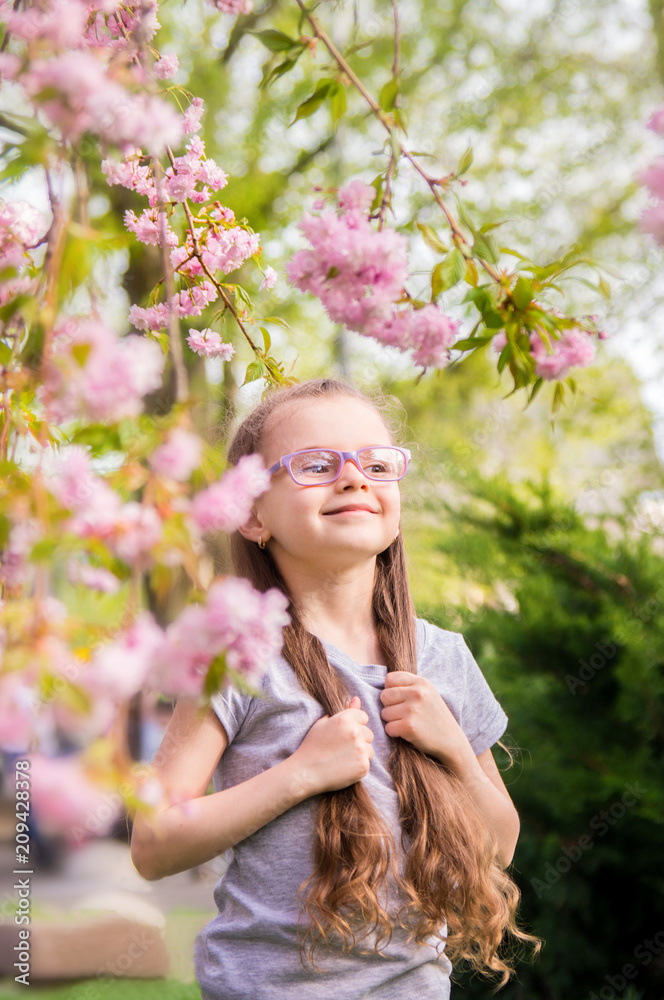 Fototapeta premium portrait of a six year old girl with glasses in a cherry blossom garden