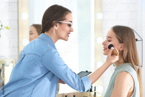 Professional visage artist applying makeup on woman's face in salon