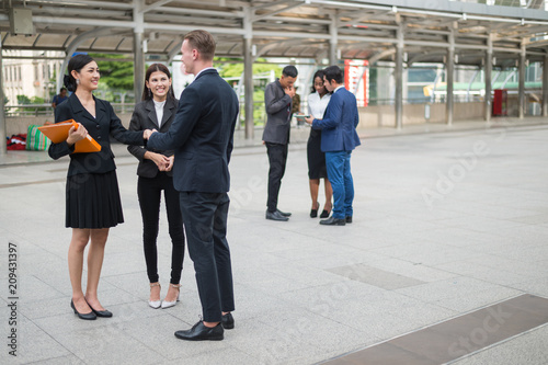 Caucasian businessman standing and shaking hand with Asian business woman and talking about business plan in the future.
