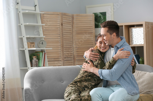 Woman in military uniform with her husband on sofa at home photo