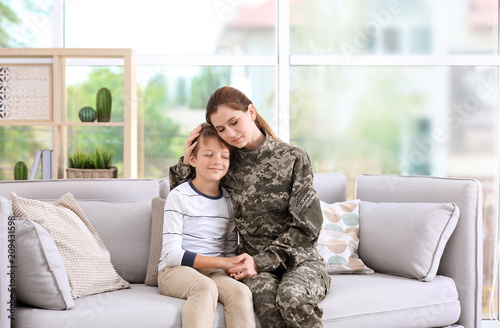 Woman in military uniform with her little son on sofa at home photo