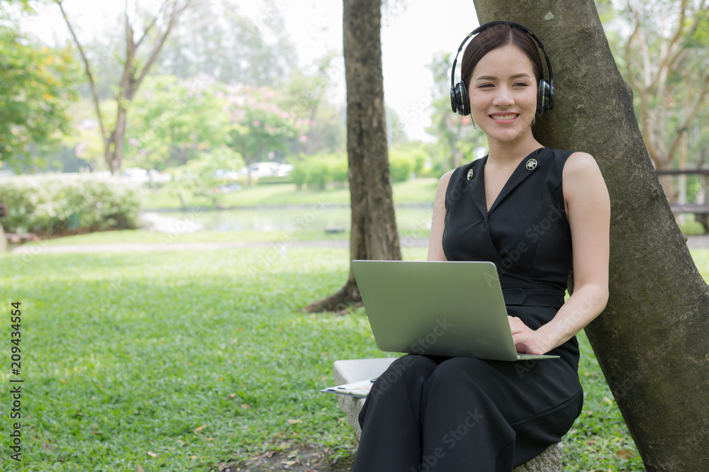 beautiful asian business woman relax by sit in the garden with laptop and listening music from stereo headset. beautiful asian business woman relax by sit in the garden with laptop and listening music from stereo headset.