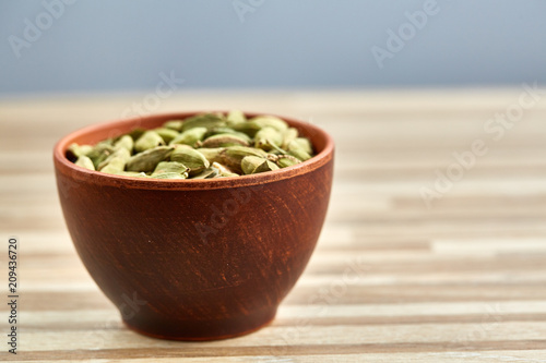 Green cardamon in ceramic bowl on wooden table close-up, top view, selective focus. photo