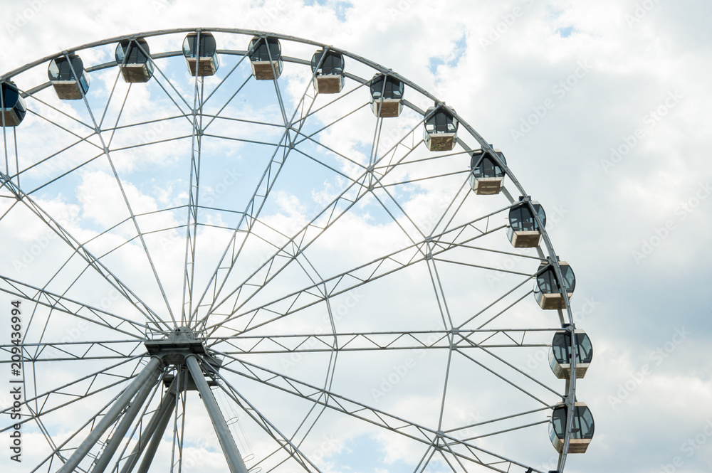 White fluffy clouds in deep blue sky, big Ferris wheel on sky background