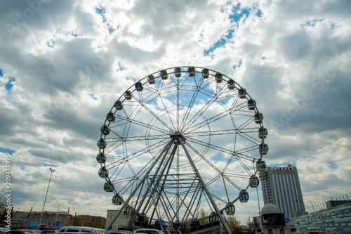 White fluffy clouds in deep blue sky, big Ferris wheel on sky background