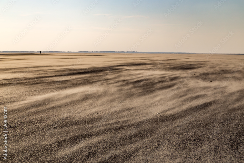 Strand von Spiekeroog bei Starkwind im Winter mit einsamer Person am Horizont Strand von Spiekeroog bei Starkwind im Winter mit einsamer Person am Horizont