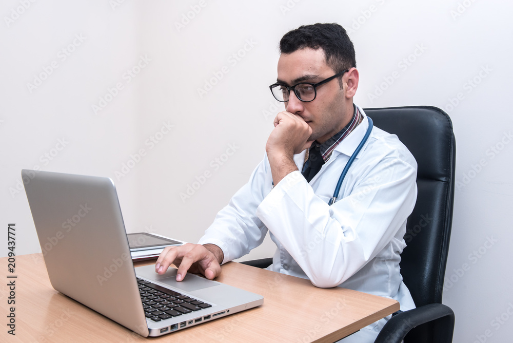 Doctor sitting at the desk, using laptop typing and searching data from the internet or searching patient record data. Doctor sitting at the desk, using laptop typing and searching data from the internet or searching patient record data.