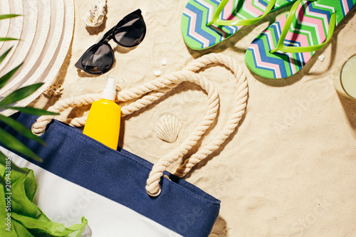 Beach accessories on the sand. Bag, colorful flip flops and hat and sunscreen. Summer vacation.