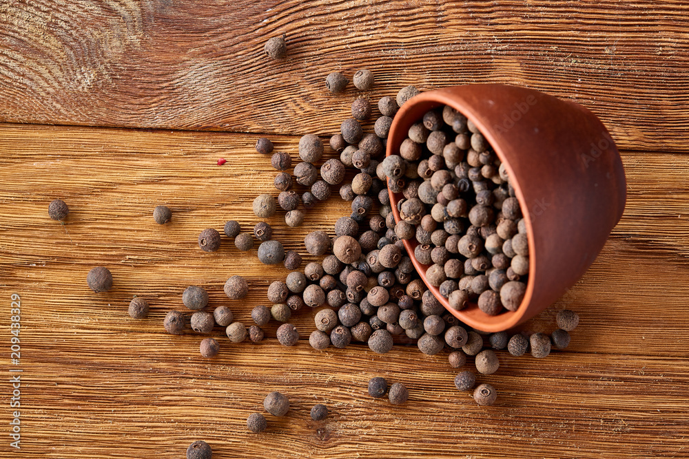 Overturned clay bowl with dried allspice berries on rustic wooden background, close-up, macro, selective focus. Overturned clay bowl with dried allspice berries on rustic wooden background, close-up, macro, selective focus.
