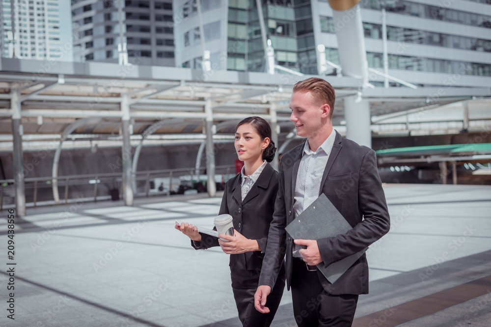 Asian business woman and Caucasian businessman walking togehter in the city and talking about business plan. Asian business woman and Caucasian businessman walking togehter in the city and talking about business plan.