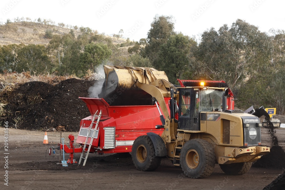 Fototapeta premium large industrial machinery being used at a garbage dump mixing and excavating green waste mulching it into compost in rural New South Wales, Australia