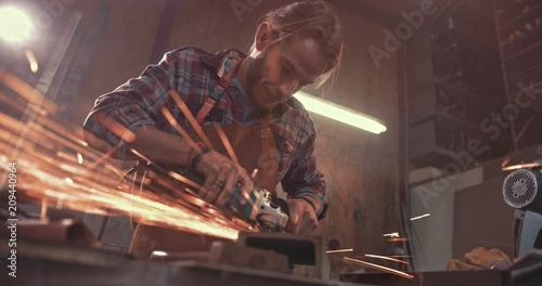 Craftsman working with metal in factory using angle grinder photo