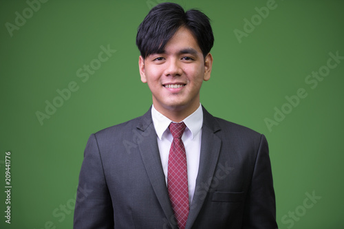 Young handsome Asian businessman against green background