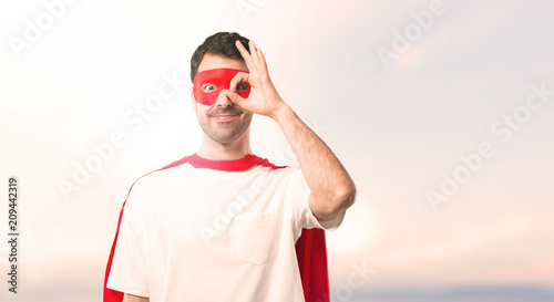 Superhero man with mask and red cape makes funny and crazy face emotion on a sunset background