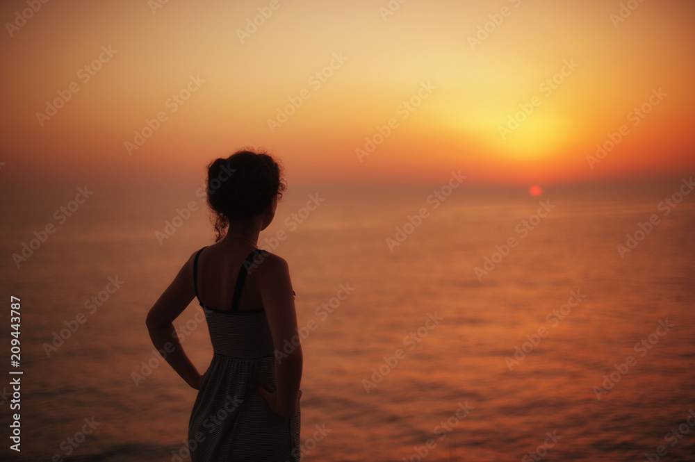 woman silhouette watching sun on the beach at sunset