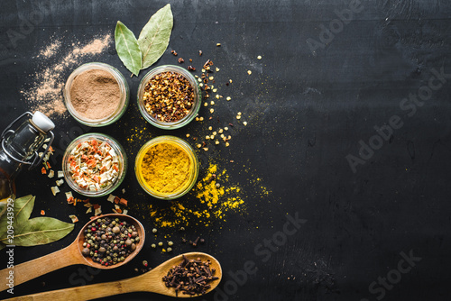 Different spices in glass and food ingredients scattered on black background