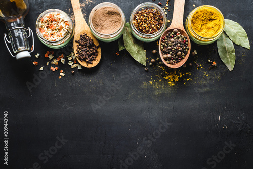 Fototapeta Naklejka Na Ścianę i Meble -  Different spices in glass and food ingredients scattered on black background