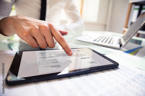 Businessperson Analyzing Invoice On Digital Tablet photo