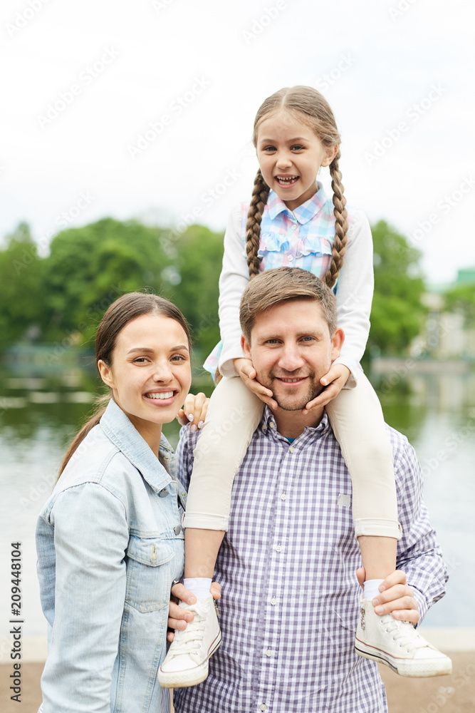 Fototapeta premium Young family in casualwear having promenade in park by waterside on summer day