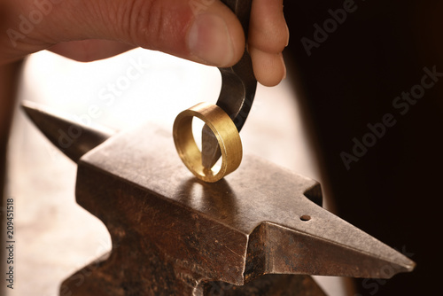 hand of a goldsmith punches a hallmark into a golden ring on an anvil, close up with copy space photo