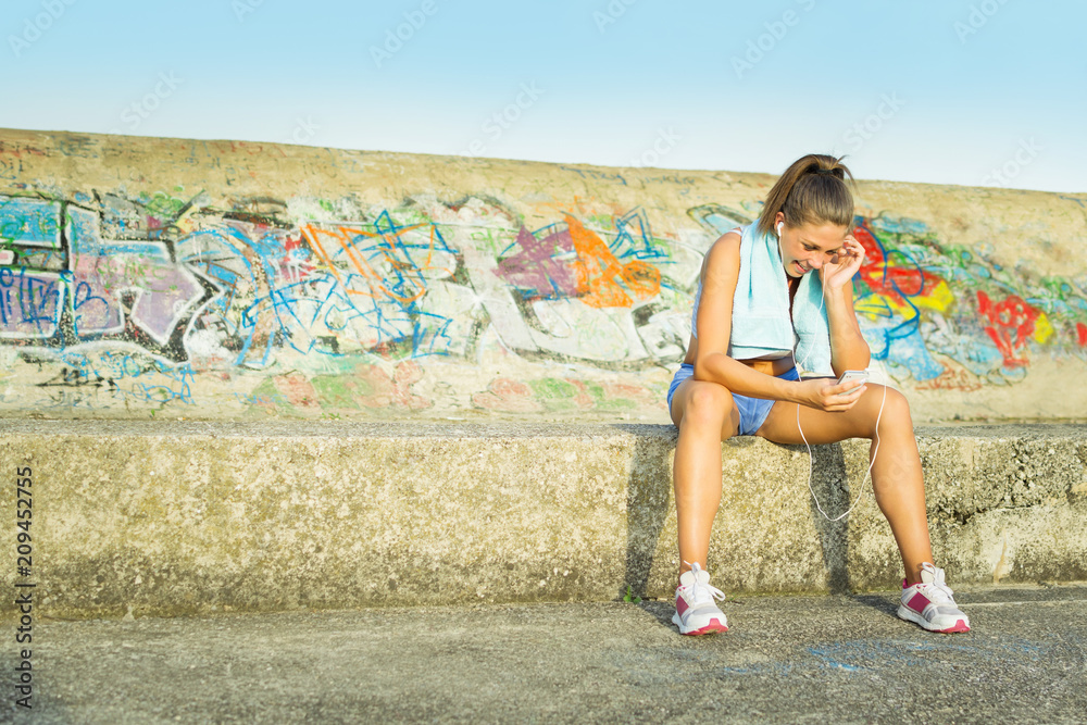 Young jogger woman sitting relaxing and listening to music after running. Natural lighting, no retouch.