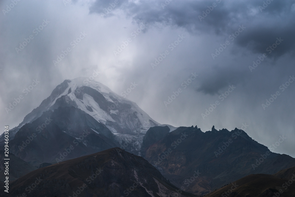 Dark rocks against background of snow-capped Kazbek mountain. Caucasian mountains. Landscape.