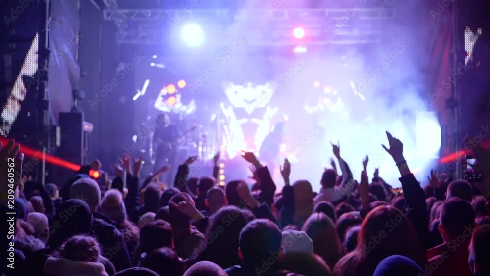 jumping fans with hands up delight of live music of rock band on bright scene in slow motion