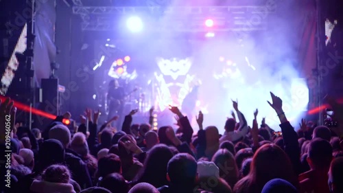 jumping fans with hands up delight of live music of rock band on bright scene in slow motion