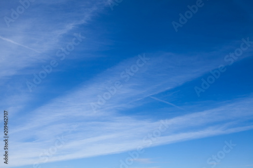 Blue sky with striped clouds. Contrail.
